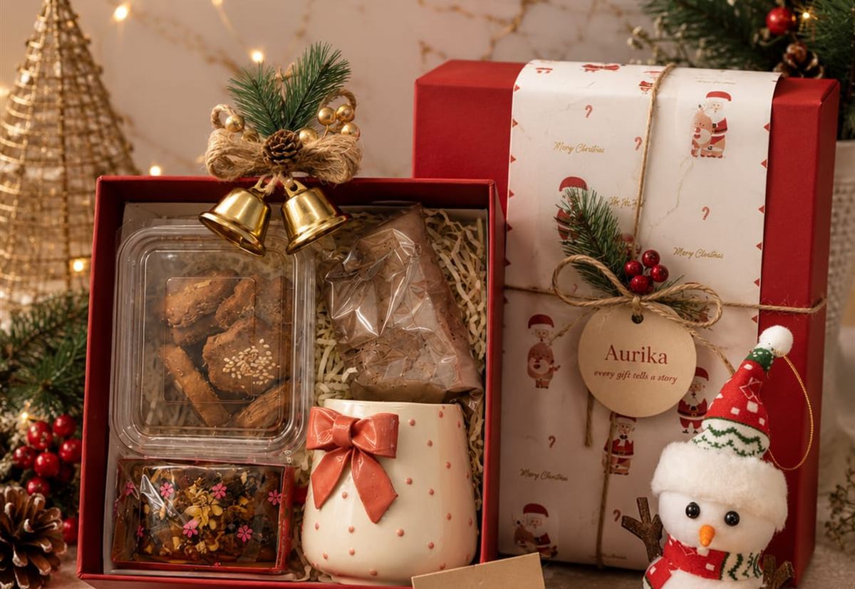 Red Christmas hamper with cookies, cocoa, a bow-handled mug, brass bells and an Aurika gift tag